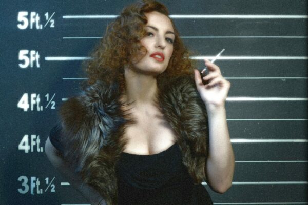 Bridget 27, artiste burlesque, posant façon mugshot rétro devant une toise avec une cigarette, photo de Henry Jee.
