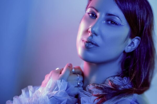 Portrait artistique de La Nanoushka, artiste burlesque, éclairée en bleu et violet avec maquillage pailleté, portant un haut en tulle vaporeux, photographiée par the Fetching Eye.