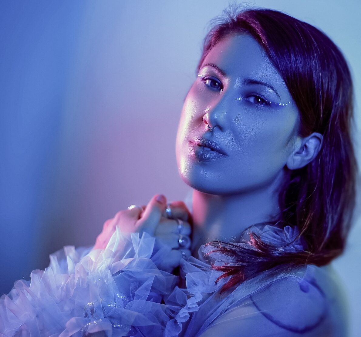 Portrait artistique de La Nanoushka, artiste burlesque, éclairée en bleu et violet avec maquillage pailleté, portant un haut en tulle vaporeux, photographiée par the Fetching Eye.