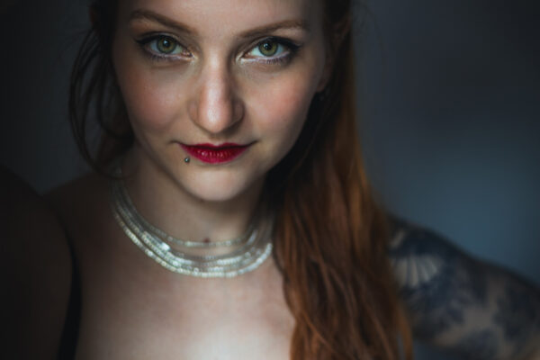 Portrait de l’artiste burlesque Ness Choucrème, photographiée par Pauline Coppe, regard intense et sourire malicieux, lumière douce et ambiance glamour.