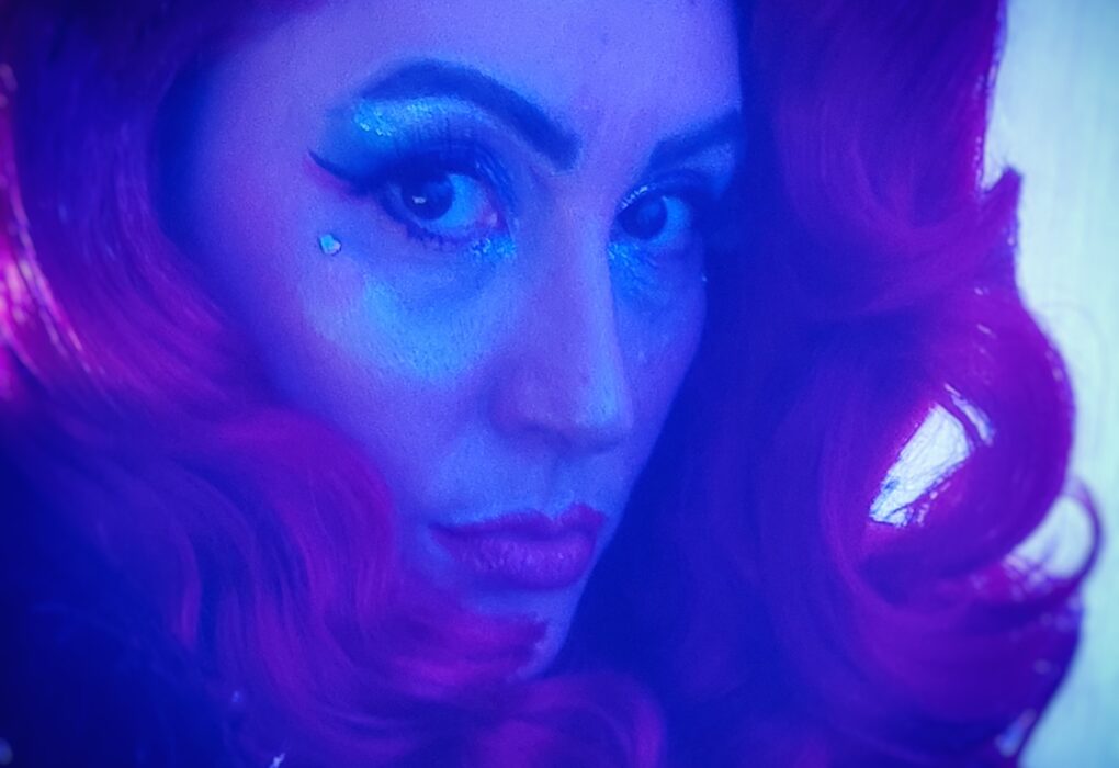 Portrait artistique d’Emeraude Plum aux cheveux ondulés violets, éclairage bleu et rose, auto-portrait burlesque.
