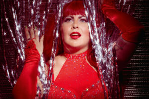 Artiste burlesque Chérie Coquette dans une tenue rouge à franges, posant devant une décoration scintillante lors d’un shooting réalisé par Jonathan-Serge Lalande.