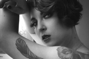 Portrait en noir et blanc de Didi Pattes de Velours, artiste burlesque, au regard intense, avec tatouage plume sur le bras. Photo Eve Saint-Ramon.