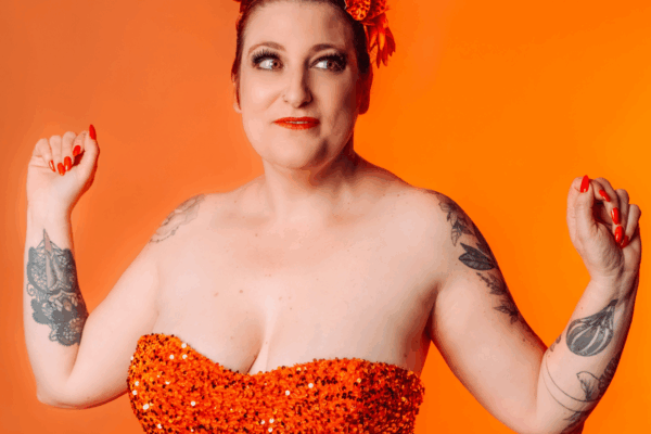 Portrait de Dotty Mac Lane, artiste burlesque française, vêtue d’un costume orange scintillant, photographiée par Studio Of Astra.