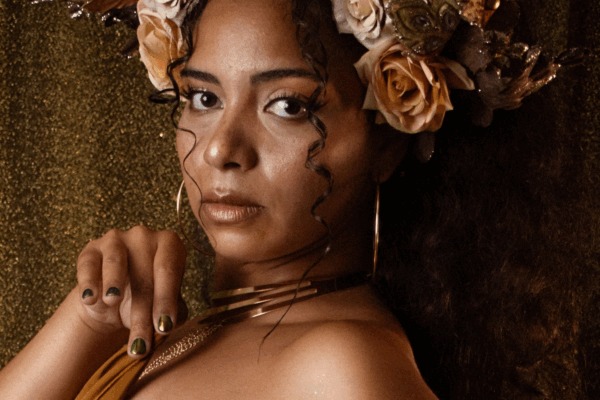 Portrait de Clarissa Velmara posant en goddess dorée, coiffée d’une couronne de fleurs et feuilles dorées, fond pailleté
