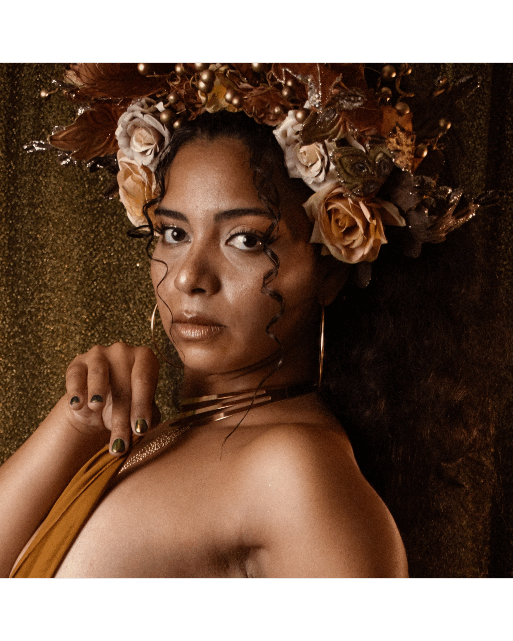 Portrait de Clarissa Velmara posant en goddess dorée, coiffée d’une couronne de fleurs et feuilles dorées, fond pailleté