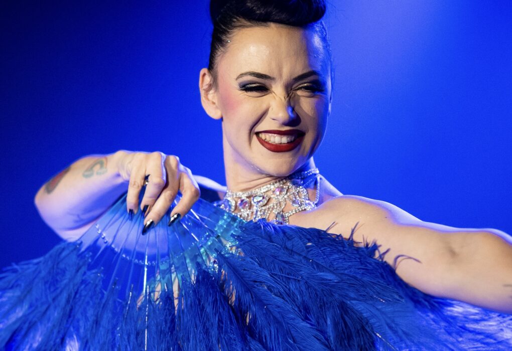 Performeur burlesque MILF Ta Mère tenant un grand éventail bleu sur scène, portrait par David Mançois.