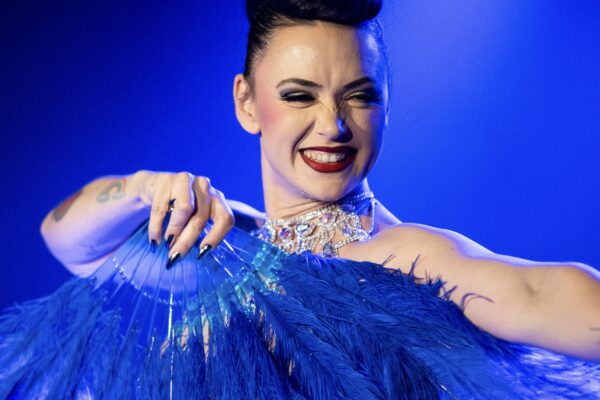 Performeur burlesque MILF Ta Mère tenant un grand éventail bleu sur scène, portrait par David Mançois.