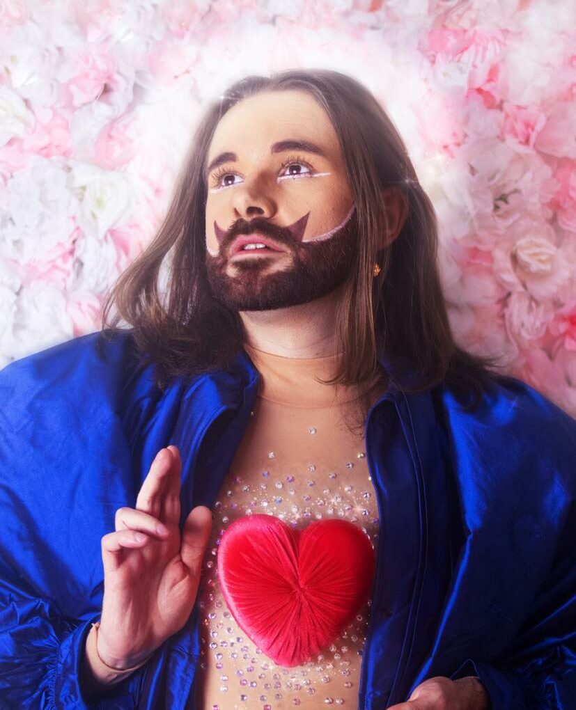 Portrait artistique d’une personne allongée sur un fond floral rose, vêtue d’un tissu bleu vif et portant un cœur rouge sur le torse.