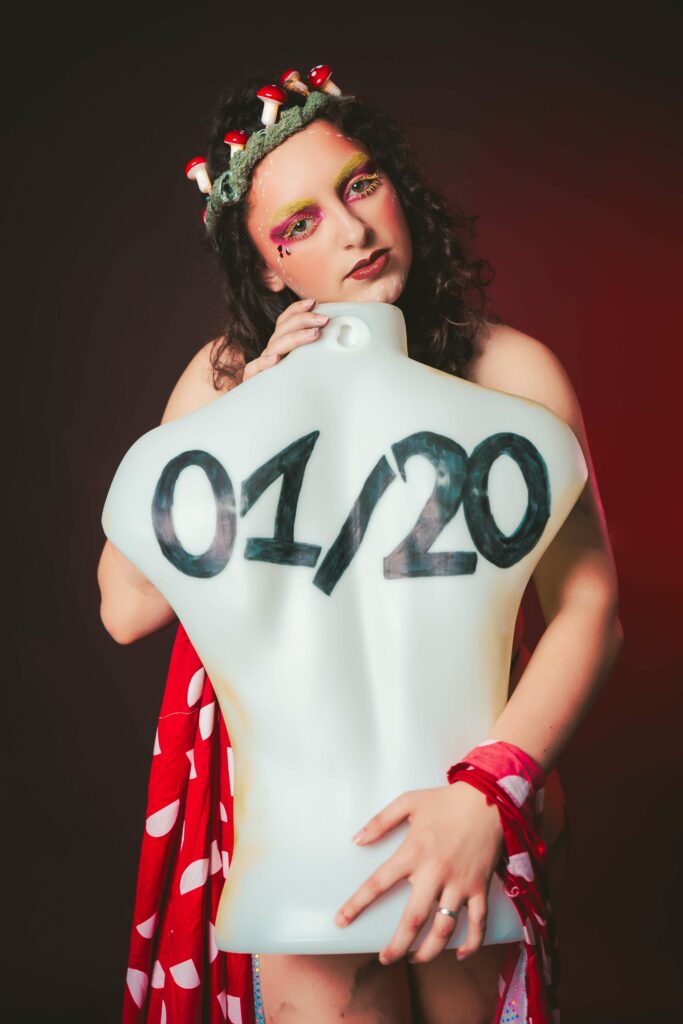 Portrait artistique de Pink Amanite avec couronne de champignons, maquillage coloré et buste blanc affichant 01/20