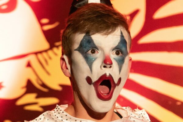 Portrait scénique de l’artiste burlesque L’innommable, vêtu d’un costume de clown contemporain serti de strass et coiffé d’un chapeau pointu, lors d’une performance haute en couleur sur scène. Crédit photo : Loraosa Pin-up.