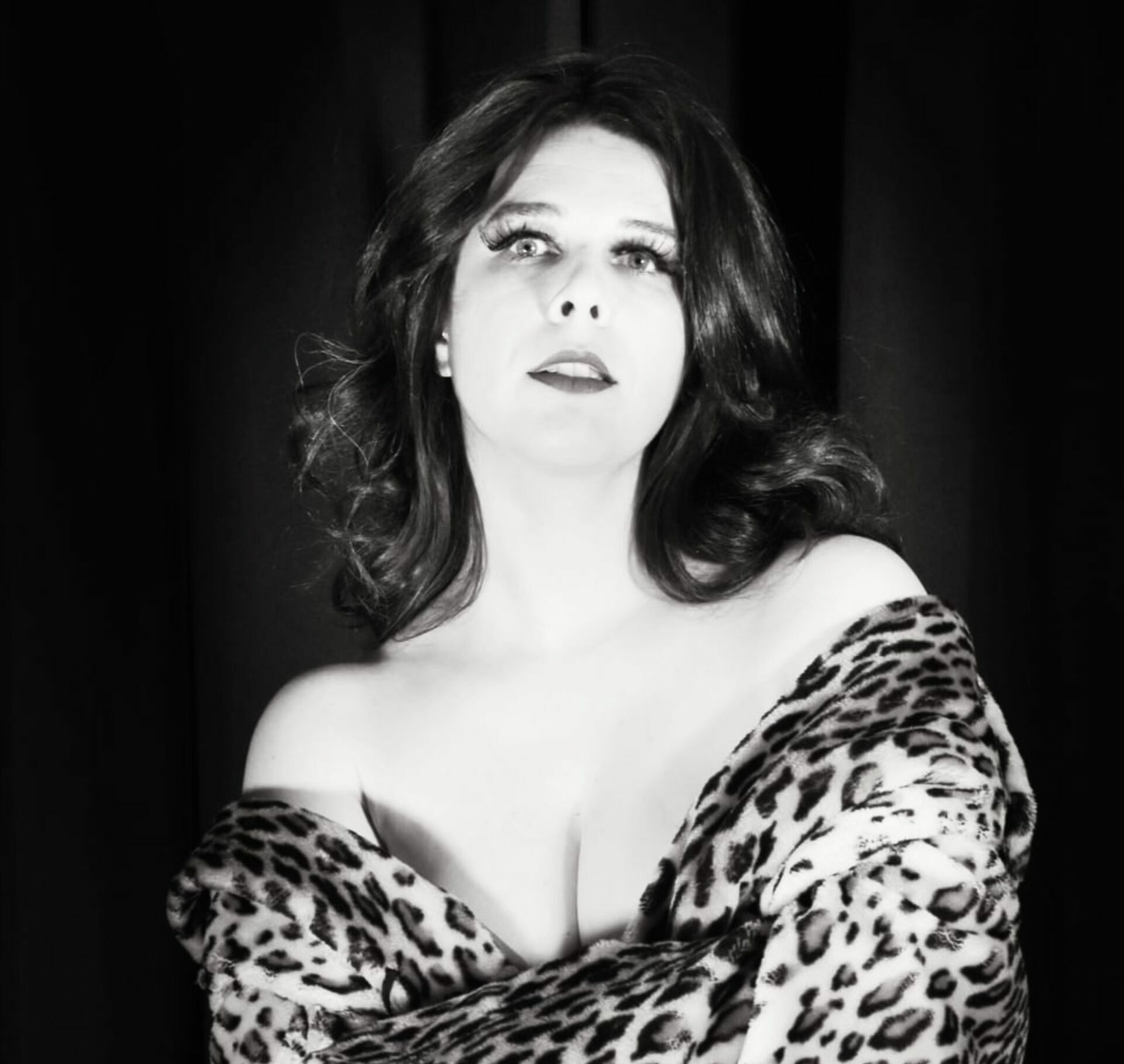 Portrait noir et blanc de Rita Noworth, artiste burlesque, de face, les épaules nues enveloppées dans un manteau à imprimé léopard, devant un fond sombre.