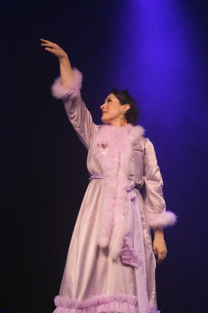 Roule Simone en pleine performance burlesque sur scène, en costume de cabaret, adoptant une pose expressive devant un décor de spectacle.