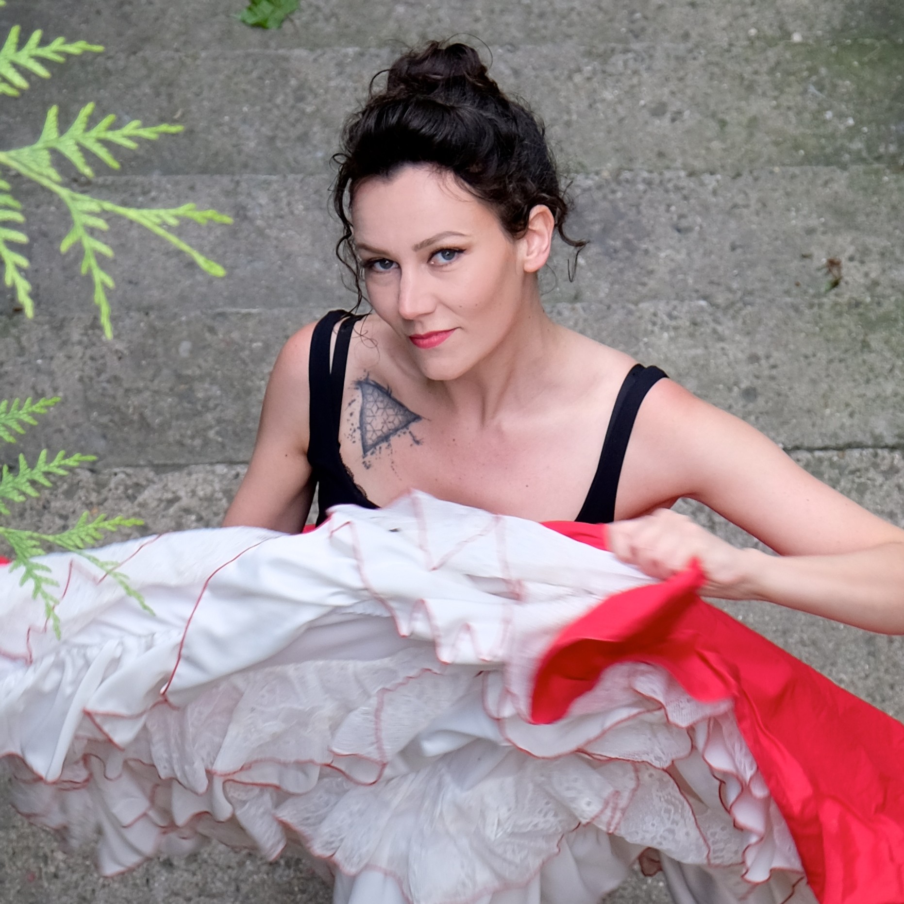 Portrait d’Andrée Gine, artiste burlesque, à l’extérieur, tenant une jupe à volants rouges et blancs, bras levés, visage partiellement tourné vers la gauche.