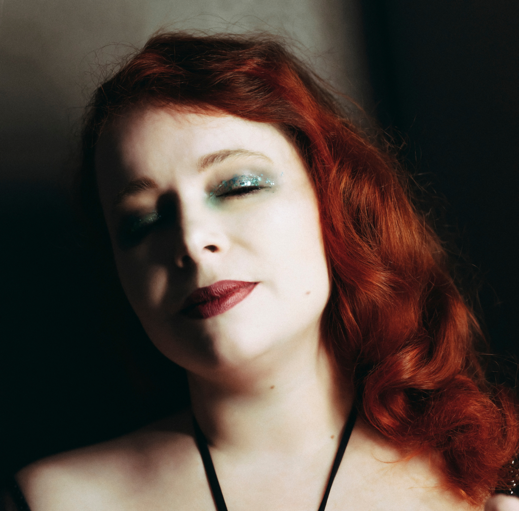 Portrait rapproché de Julie Crève-Coeur mettant en valeur ses cheveux roux ondulés et son décolleté dans un costume de scène noir.