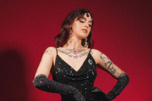 Lady Luciole en robe longue noire pailletée, gants longs et talons, posant sur fond rouge, silhouette glamour burlesque – Photo Veronica Marxx