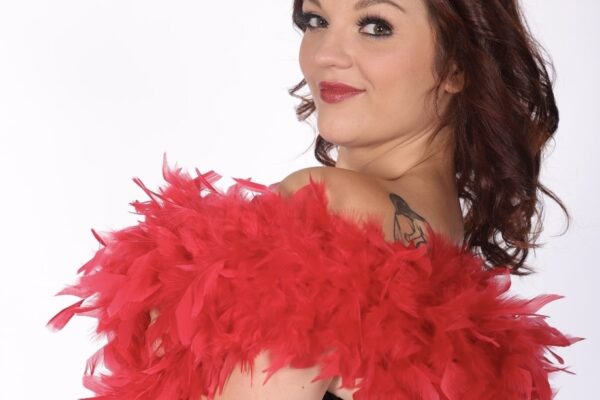 Portrait de l’artiste burlesque Stella Luna de trois quarts, portant un corset noir et rouge et un boa de plumes rouges, photographiée par kumasmile88_photo_courchevel.