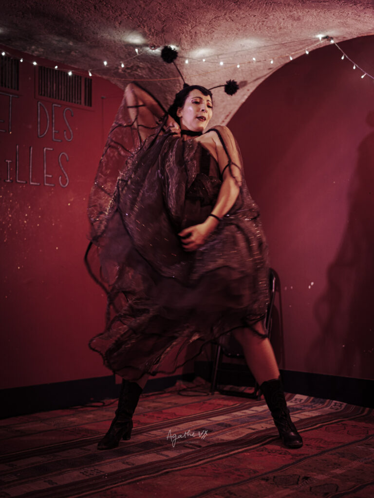 Artiste burlesque Eva La Vamp en pleine performance, robe vaporeuse en mouvement sur une petite scène, photographiée dans une ambiance lumineuse rouge.