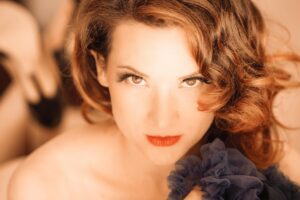 Portrait serré de l’artiste burlesque Marie Tournelle, regard direct vers l’objectif, tenant un tissu bleu foncé, photographiée par Laurent Qy.