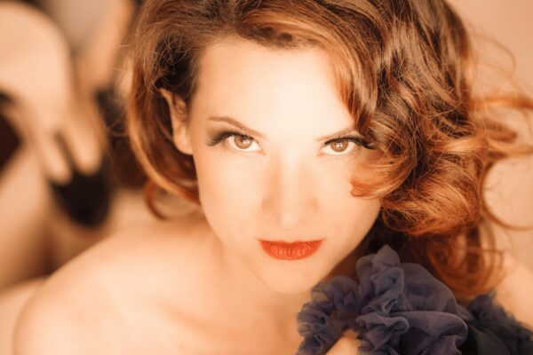 Portrait serré de l’artiste burlesque Marie Tournelle, regard direct vers l’objectif, tenant un tissu bleu foncé, photographiée par Laurent Qy.