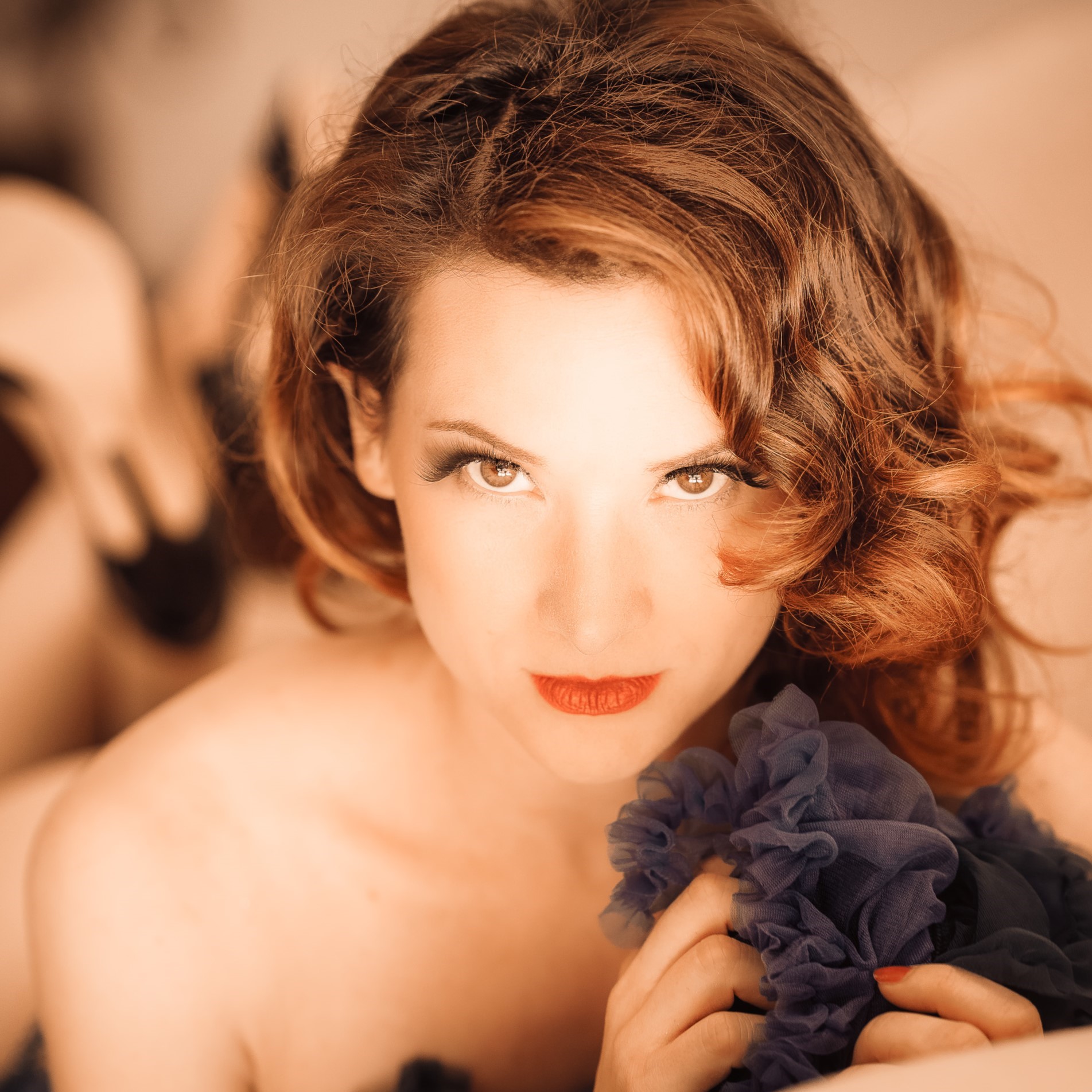 Portrait serré de l’artiste burlesque Marie Tournelle, regard direct vers l’objectif, tenant un tissu bleu foncé, photographiée par Laurent Qy.