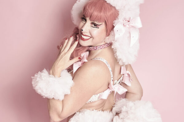Rosabelle Sélavy de dos en costume burlesque rose et blanc inspiré d’un caniche, posant devant un fond rose en studio, photographiée par Studio Volua à Paris.