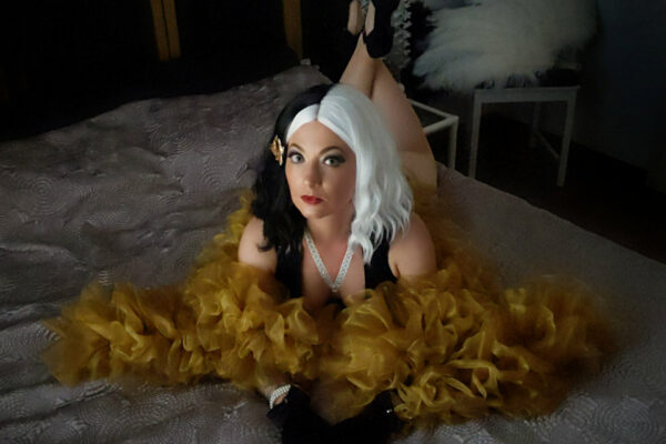 Portrait Daâr Djiling artiste burlesque alsacienne cheveux bicolores noir blanc plumes jaunes sur lit sombre