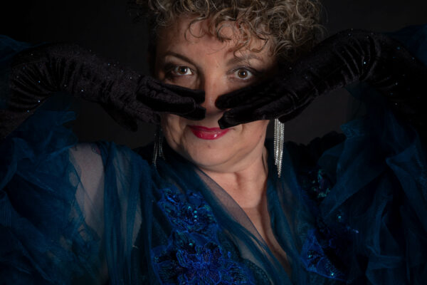 Lady Poppy Scarlett, artiste burlesque, cheveux bouclés blancs, gants noirs couvrant visage, robe bleue brodée. Photographe : Cécile Schwaller.