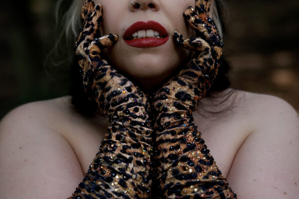Artiste burlesque Mimi Oh La La portant de longs gants léopard pailletés, posant en gros plan dans un décor de forêt