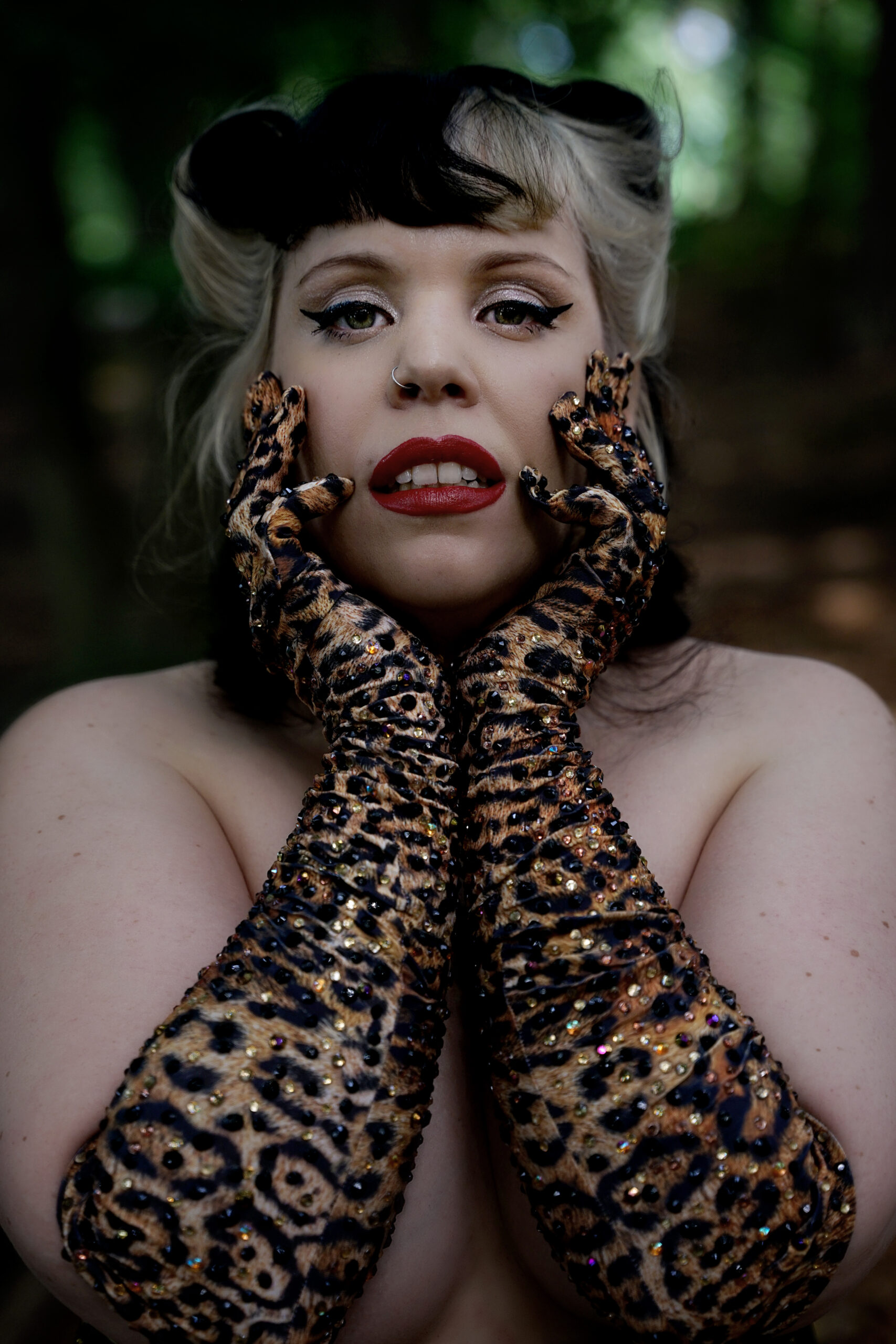 Artiste burlesque Mimi Oh La La portant de longs gants léopard pailletés, posant en gros plan dans un décor de forêt