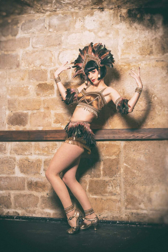 Enveloppe Timbrée artiste burlesque en costume plumes et franges dorées posant de profil contre un mur de pierred’oreilles longues