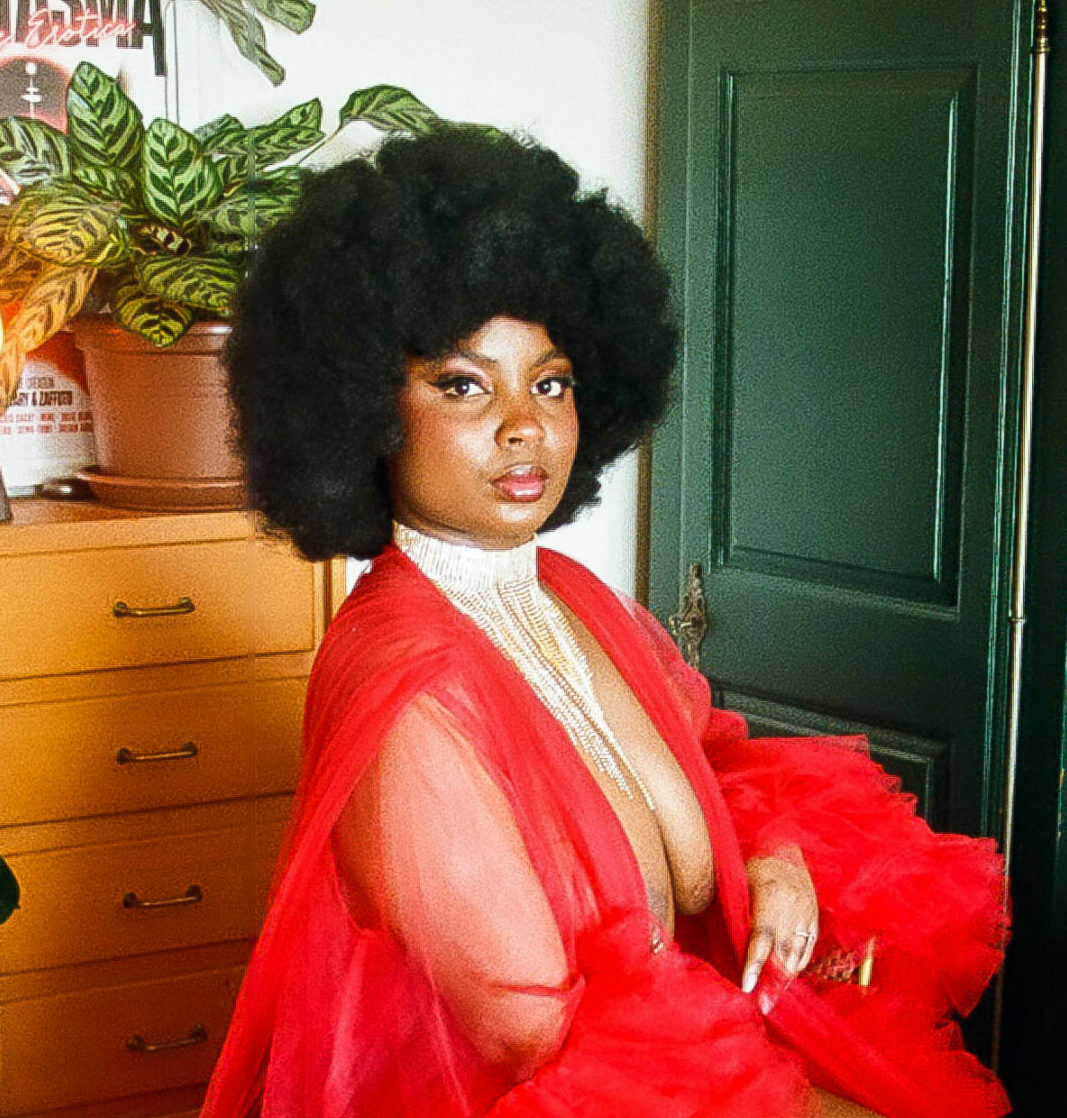 Nubsaphrodite, artiste burlesque, en kimono rouge transparent et chevelure afro, décor plantes et poster Fantasma.