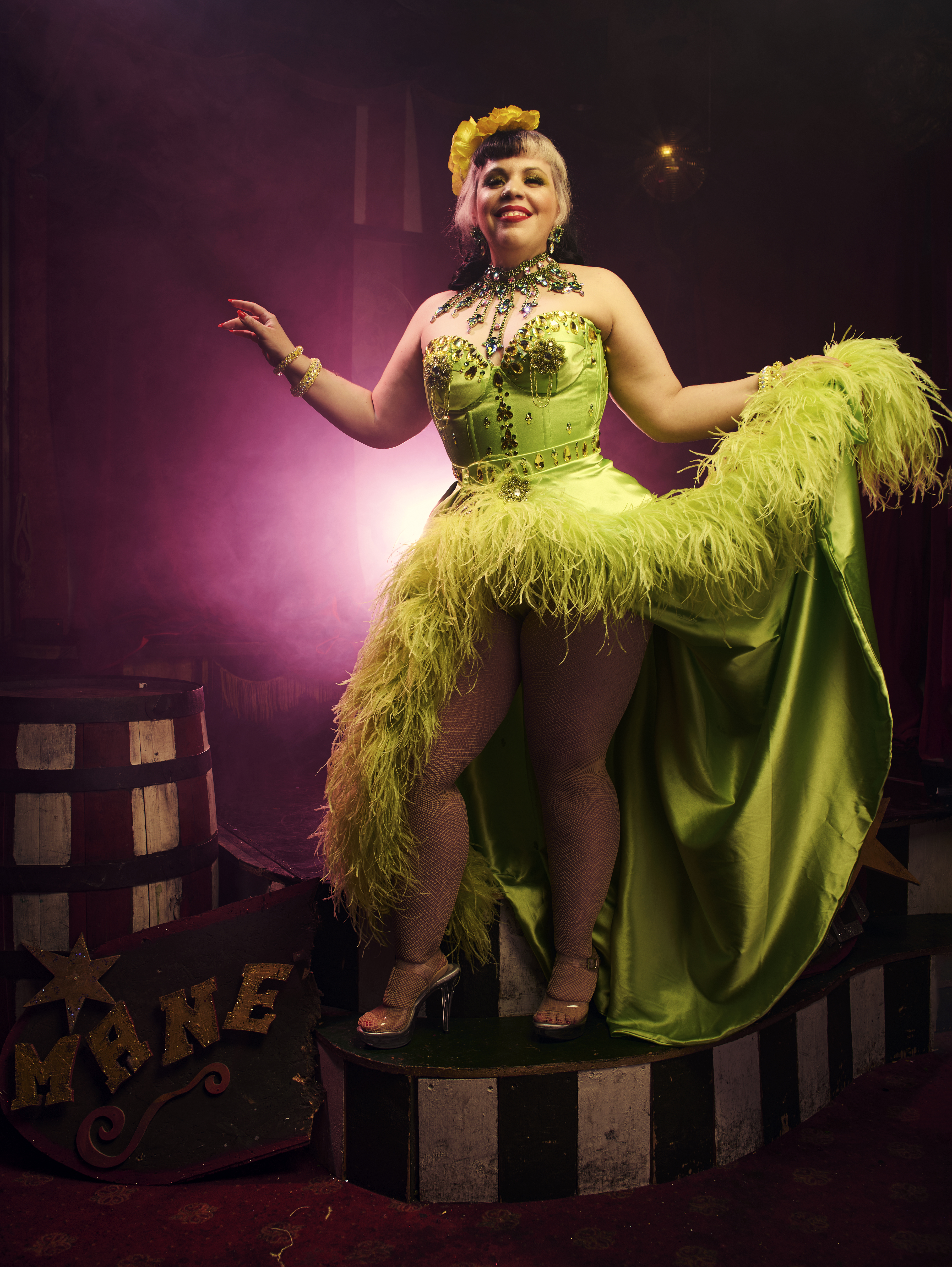 Artiste burlesque Mimi Oh La La en robe verte à plumes, posant sur scène dans une ambiance de cabaret avec lumière rose