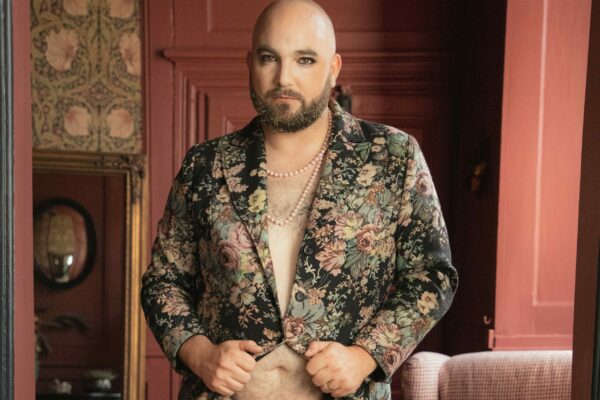 Portrait Monsieur Paul Piette, artiste burlesque, veste fleurie ouverte et slip doré, fond rouge.