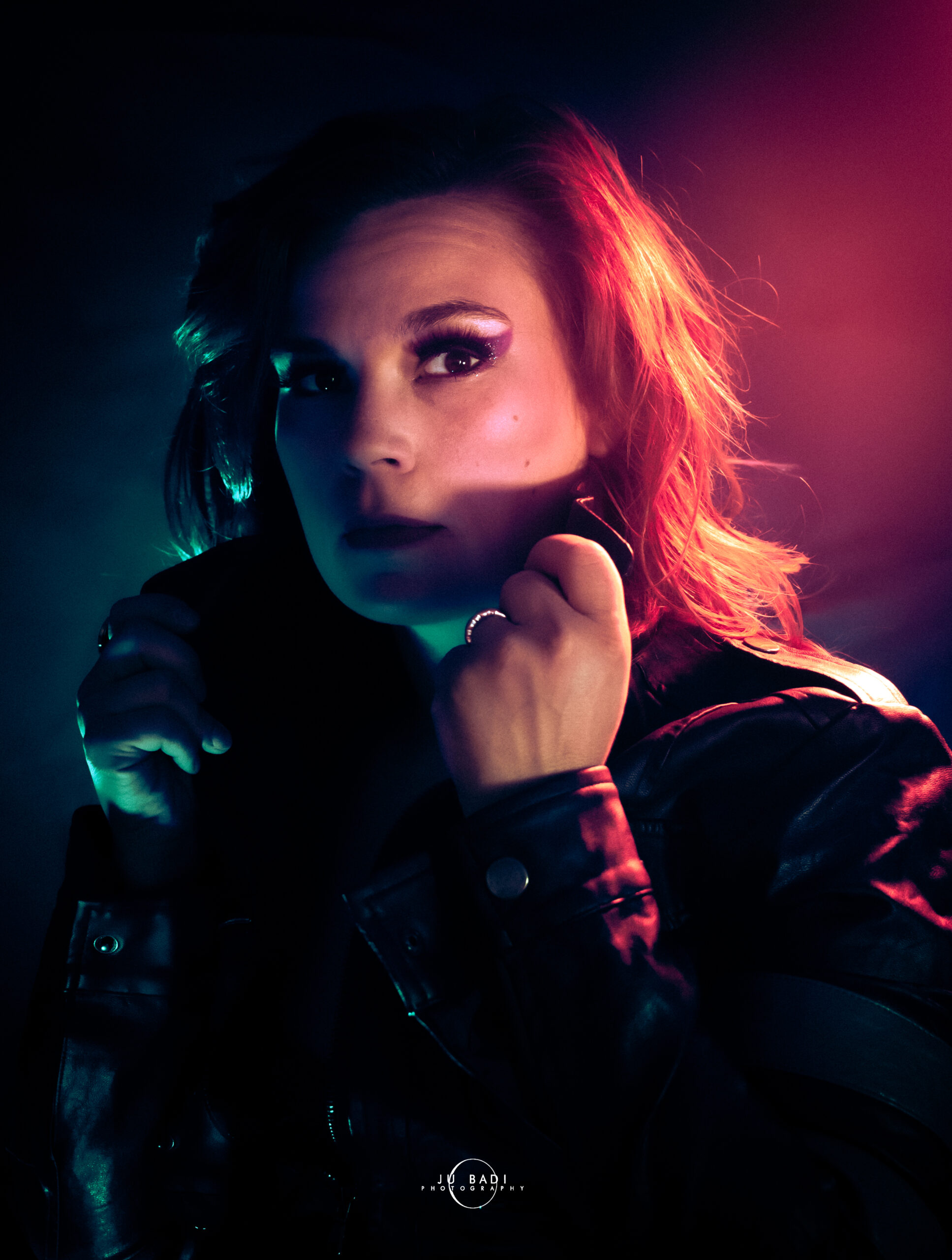 Patti Bear, artiste burlesque rousse, veste cuir noire éclairage néon violet rose, regard intense. Photographe : Jubadi Photography