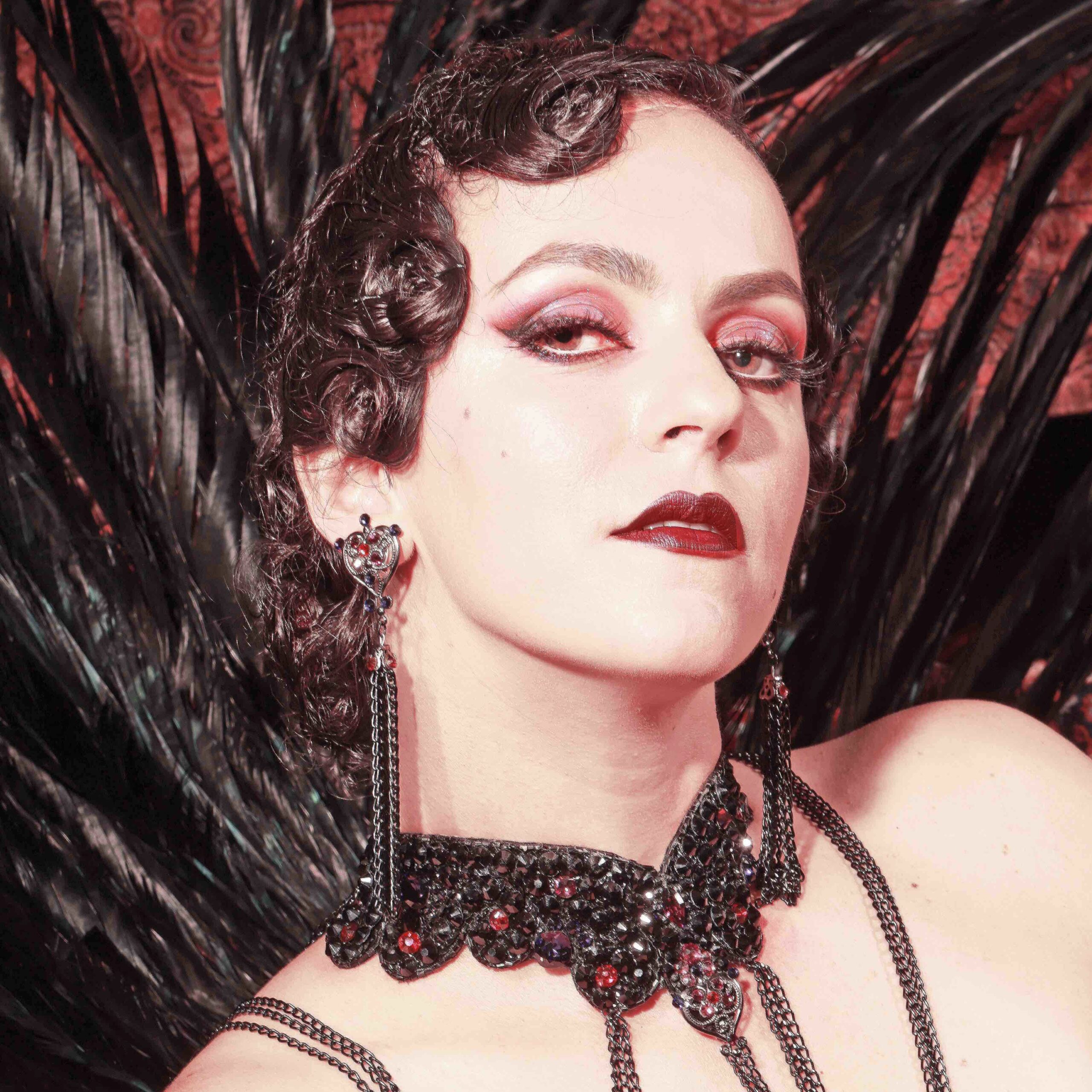 Portrait Velena Rossa style rétro 1920s, coiffure ondulée noire collier chaînes noires lèvres rouges. Crédit photo : Neil Kendall