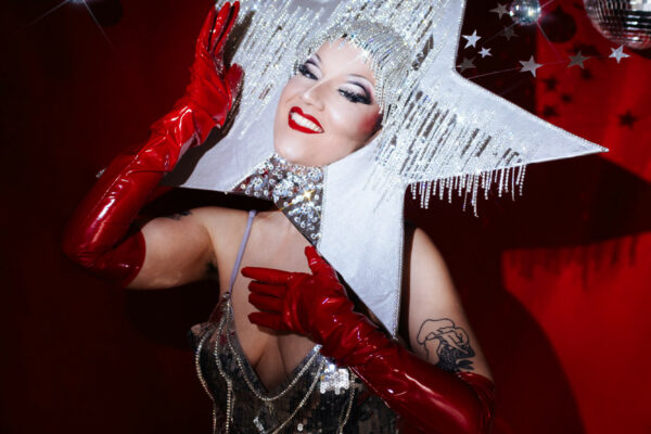 Hot Headed Christine, performeuse mutante, robe paillettes argent star géante gants rouges fond étoiles rouges.