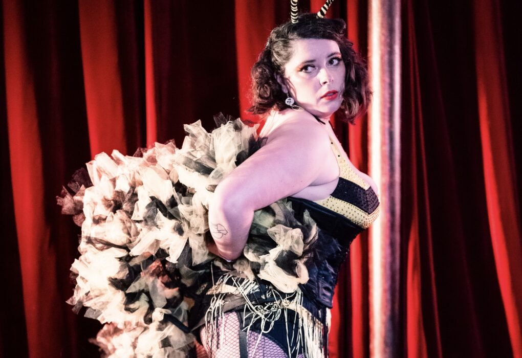 Lulu Toute Crue artiste burlesque ronde costume noir plumes blanches rayures jarretières sur scène cabaret