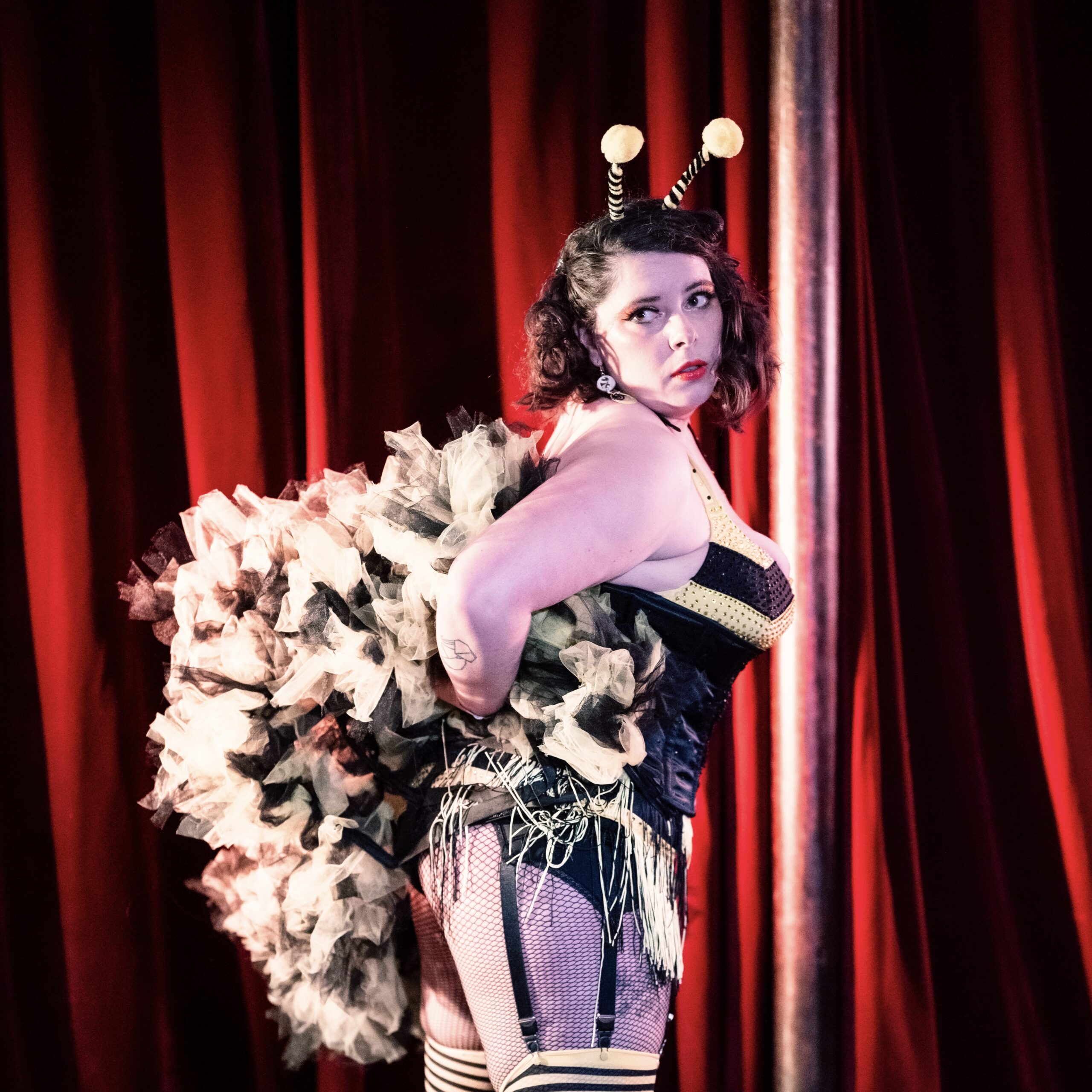 Lulu Toute Crue artiste burlesque ronde costume noir plumes blanches rayures jarretières sur scène cabaret