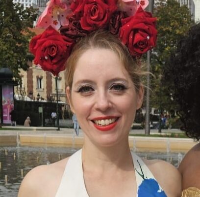Ondine Désiles, artiste burlesque, couronne roses rouges, robe fleurie blanche bleue rouge devant skyline urbain.