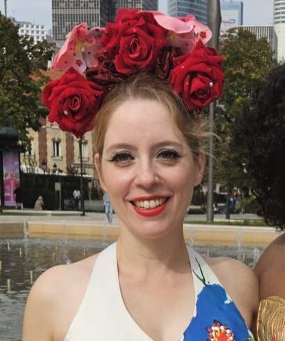 Ondine Désiles, artiste burlesque, couronne roses rouges, robe fleurie blanche bleue rouge devant skyline urbain.
