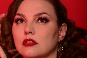 Portrait Sucre à la Crème effeuilleuse burlesque Montréal fond rouge lèvres rouges boucles d’oreilles pendantes