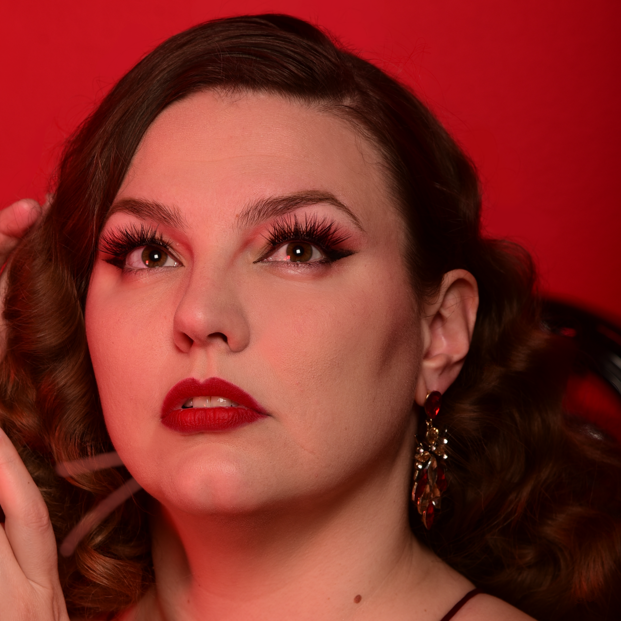 Portrait Sucre à la Crème effeuilleuse burlesque Montréal fond rouge lèvres rouges boucles d’oreilles pendantes