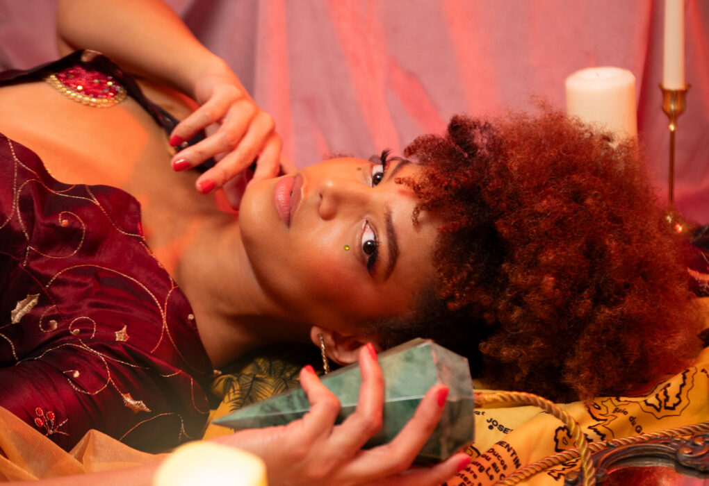 Portrait de l'artiste burlesque Jade Orlys allongée dans une ambiance mystique avec un cristal et des bougies. Photo par Loraosa Pin-Up.