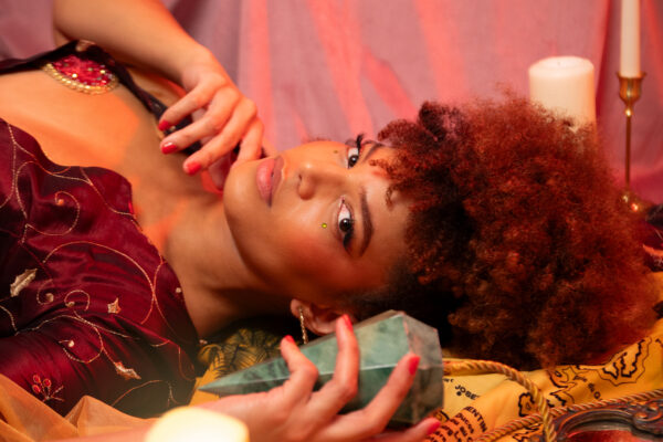 Portrait de l'artiste burlesque Jade Orlys allongée dans une ambiance mystique avec un cristal et des bougies. Photo par Loraosa Pin-Up.